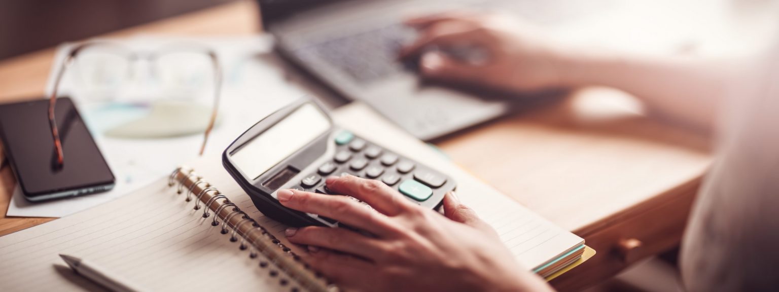 Woman working with laptop and calculator at home office. Close-up panoramic view. Concept of the freelancer.